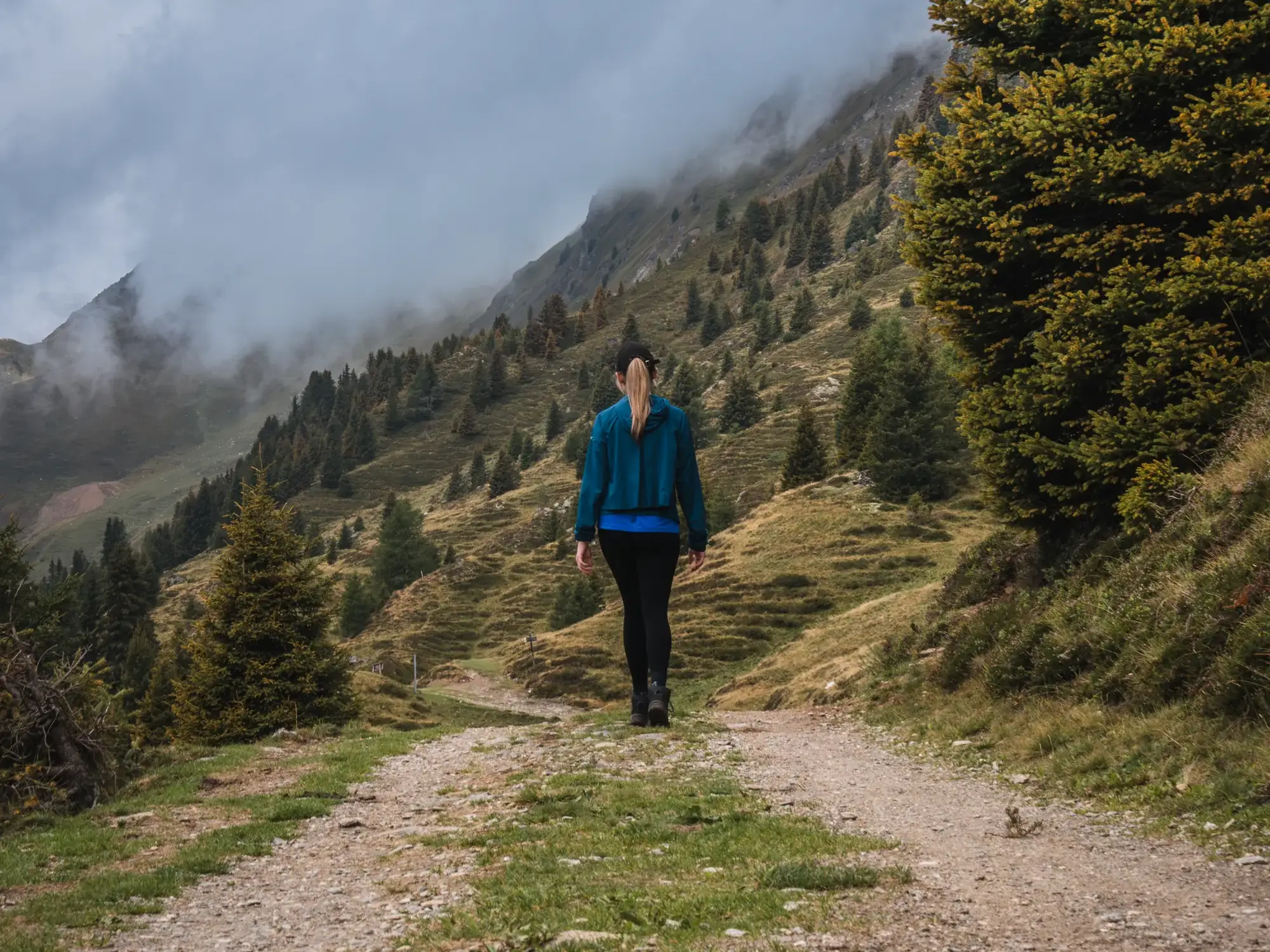 Wanderin auf einem Bergweg, Nebel zieht über die Hänge im Hintergrund